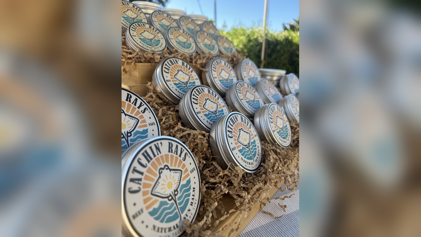 Stacked tins of Catchin' Rays natural sun balm with an orange sunburst and stingray logo