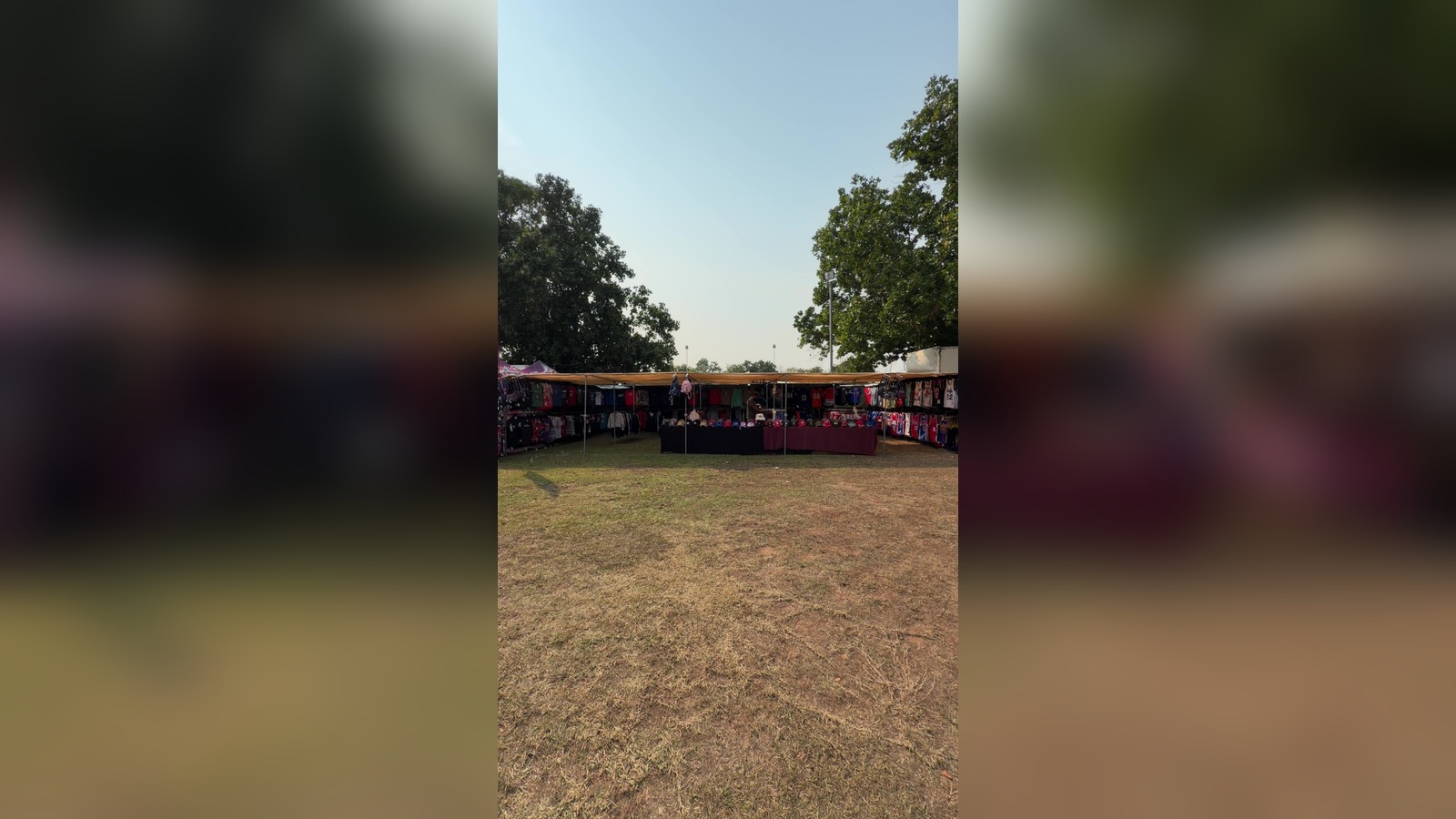 Wide view of a sportswear stall under a shade tent with racks of printed t-shirts and rows of caps on tables